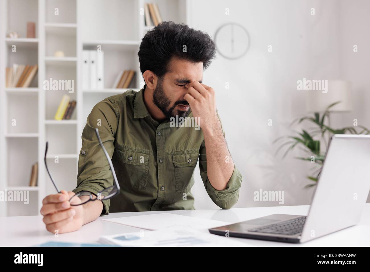 L'indiano stanco si toglie gli occhiali, soffre di sensazioni dolorose, ha problemi con l'astigmatismo. Un uomo stressato dopo una lunga giornata di lavoro al Foto Stock