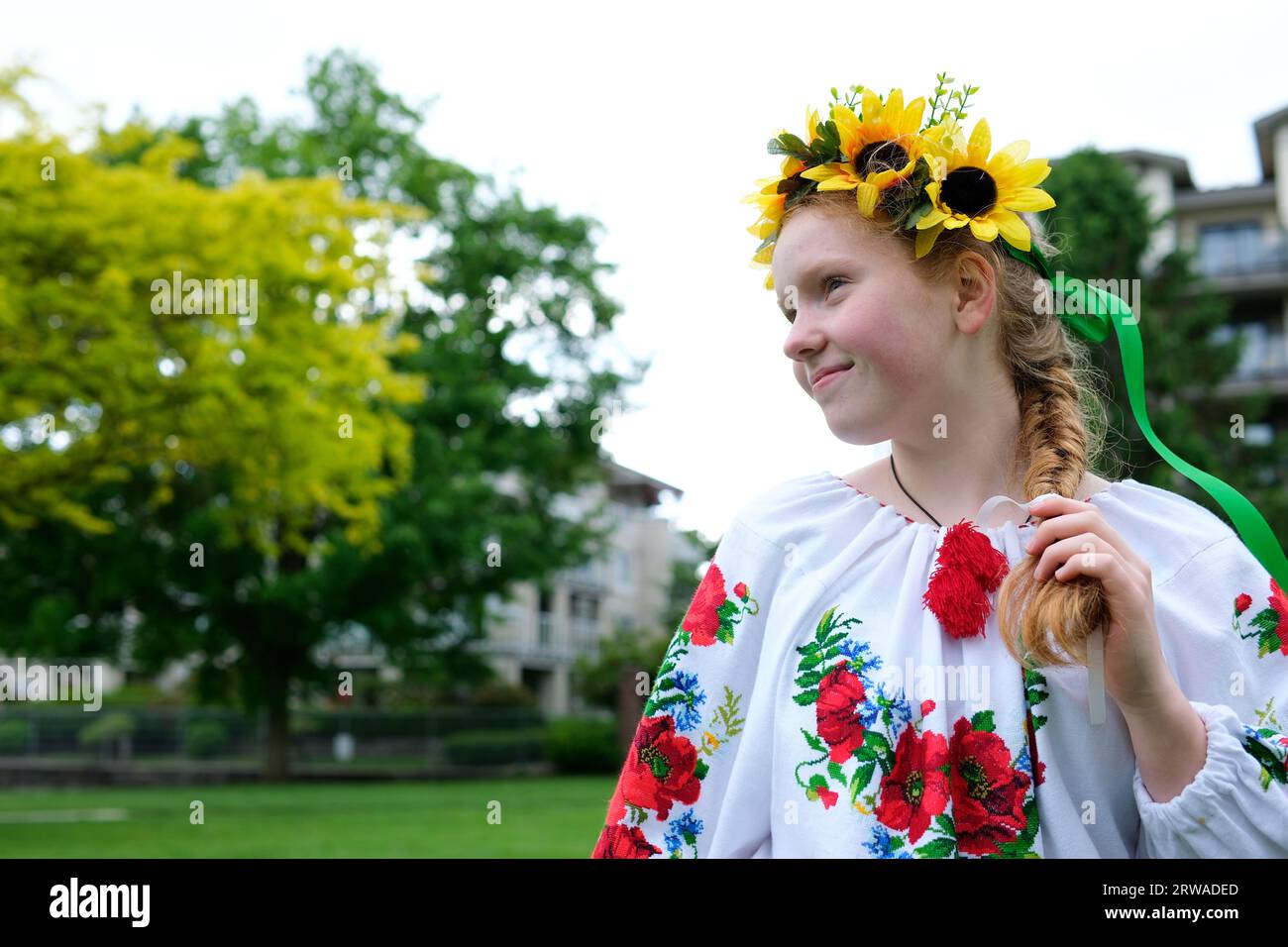 Bella ragazza Ucraina dai capelli rossi in una camicetta ricamata fiori di papaveri rossi su una camicia bianca corona di girasoli nei suoi nastri di capelli frequenza della natura forza di bellezza vergine. Vittoria gioia pace Foto Stock
