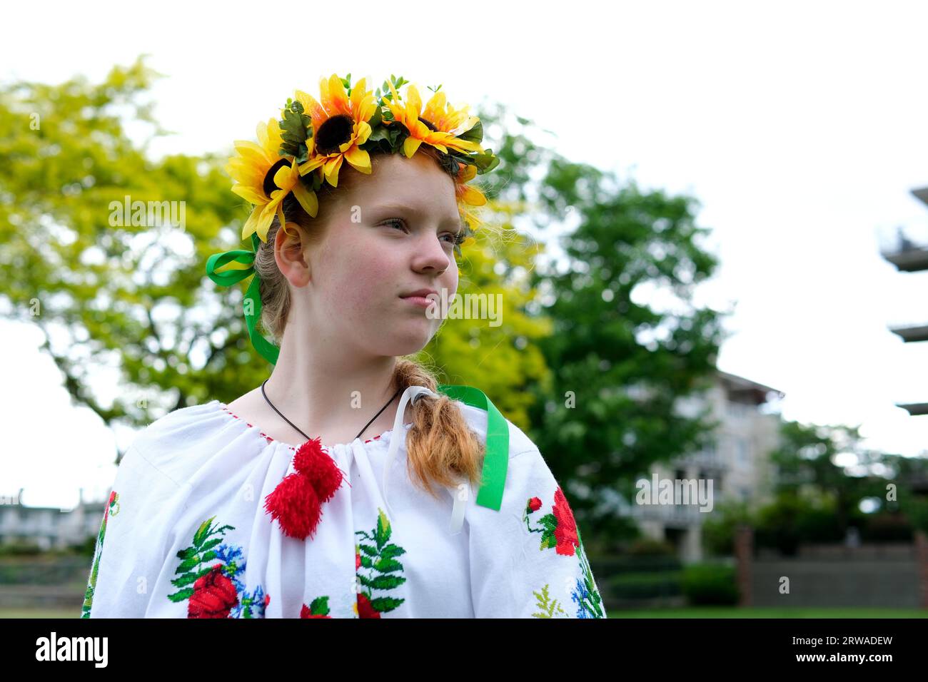 Bella ragazza Ucraina dai capelli rossi in una camicetta ricamata fiori di papaveri rossi su una camicia bianca corona di girasoli nei suoi nastri di capelli frequenza della natura forza di bellezza vergine. Vittoria gioia pace Foto Stock