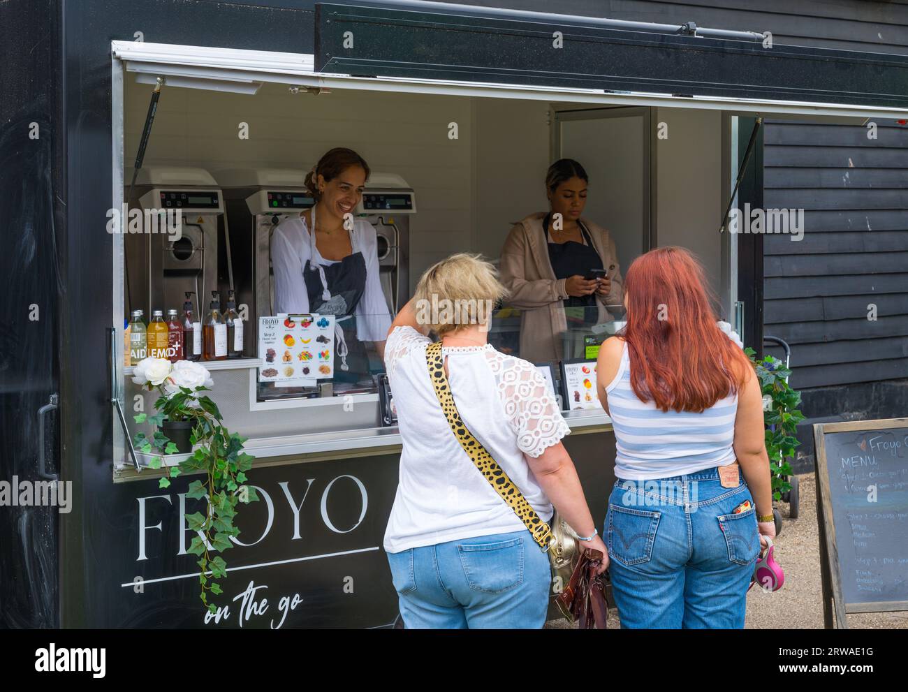 Due donne che acquistano yogurt congelato da Froyo On the Go van al mercato dell'artigianato e del cibo di Duckpond Market. Ruislip, Middlesex, Inghilterra, Regno Unito Foto Stock