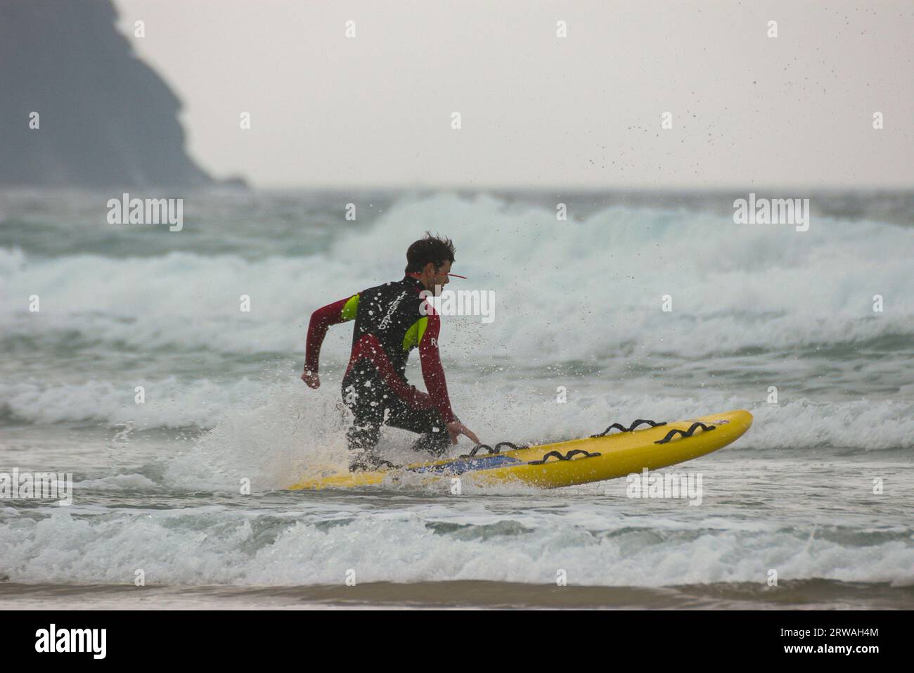 Membro del bagnino RNLI con bordo di salvataggio da surf in direzione di mari irregolari al largo di Perranporth Beach, Cornovaglia, Regno Unito. Foto Stock