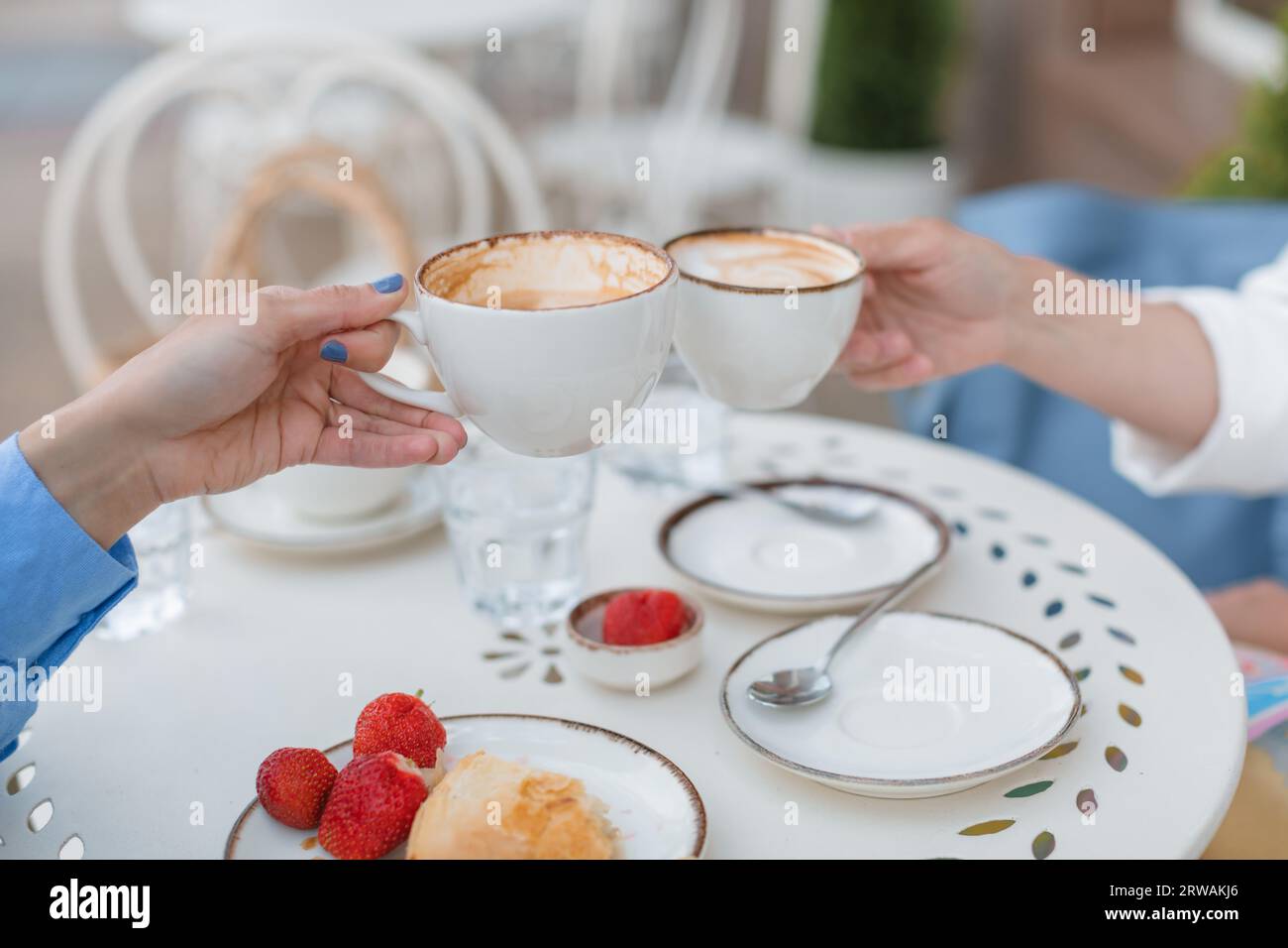 Due donne sedute fuori da un caffè che brindano con tazze di caffè Foto Stock