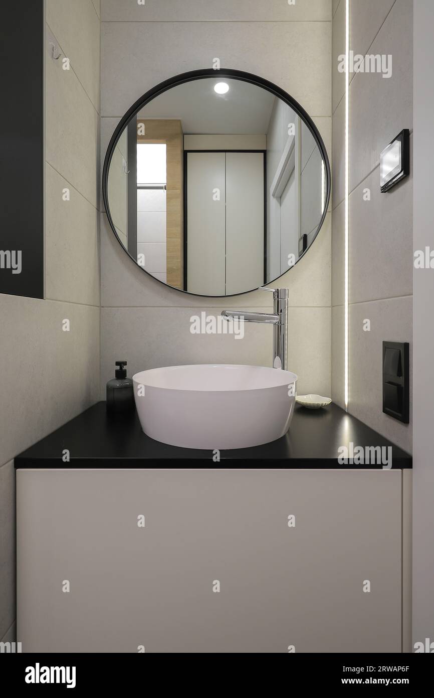 Rubinetto con lavandino in ceramica e specchio rotondo all'interno del bagno Foto Stock Rubinetto con lavandino in ceramica e specchio rotondo all'interno del bagno Foto Stock