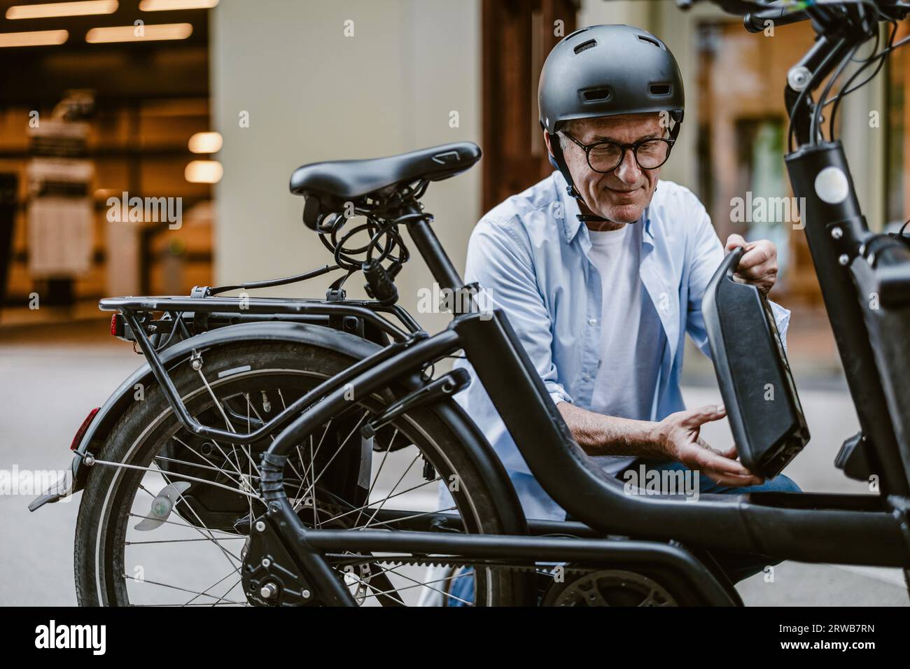 Uomo anziano che cambia la batteria su una bicicletta elettrica Foto Stock