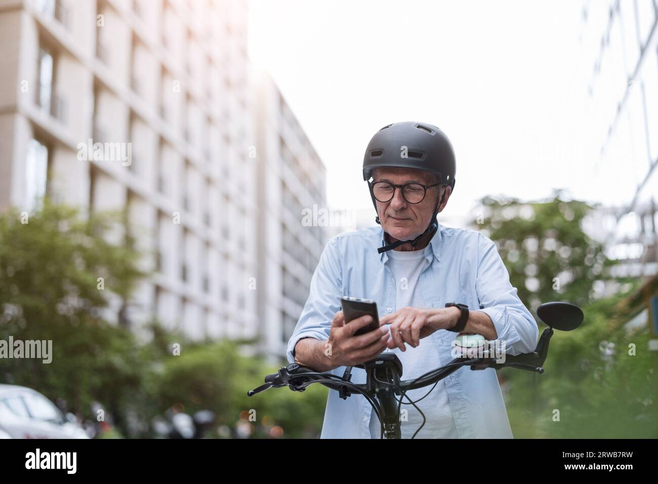Uomo maturo che usa il telefono cellulare mentre si va in bicicletta in città Foto Stock