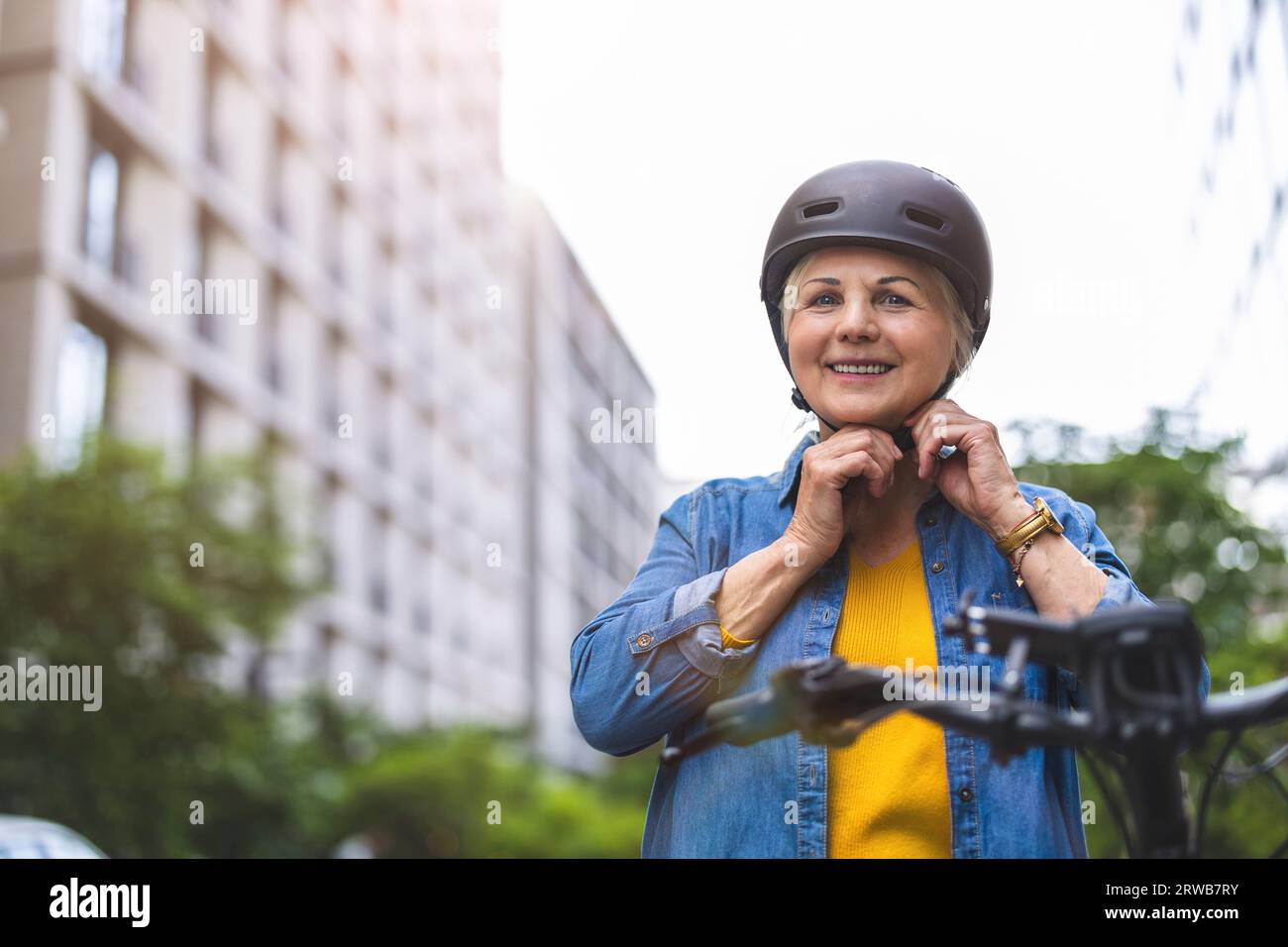Ritratto di una donna anziana che indossa il casco mentre si va in bicicletta in città Foto Stock