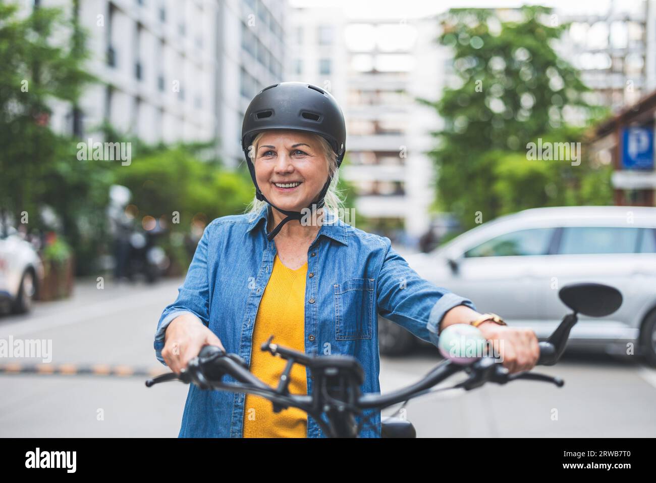 Ritratto di una donna anziana che indossa il casco mentre si va in bicicletta in città Foto Stock