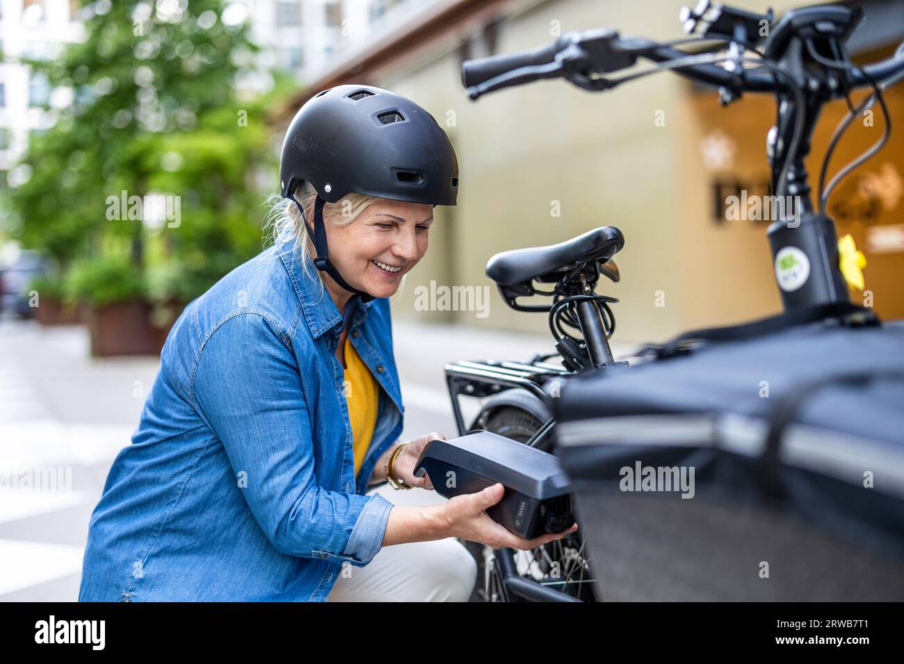 Donna matura che cambia la batteria su una bicicletta elettrica Foto Stock