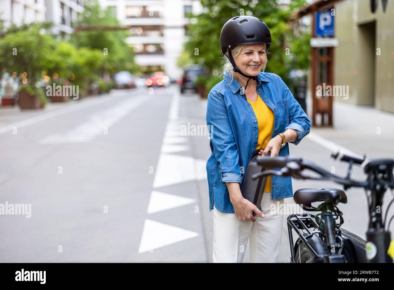 Donna matura che cambia la batteria su una bicicletta elettrica Foto Stock