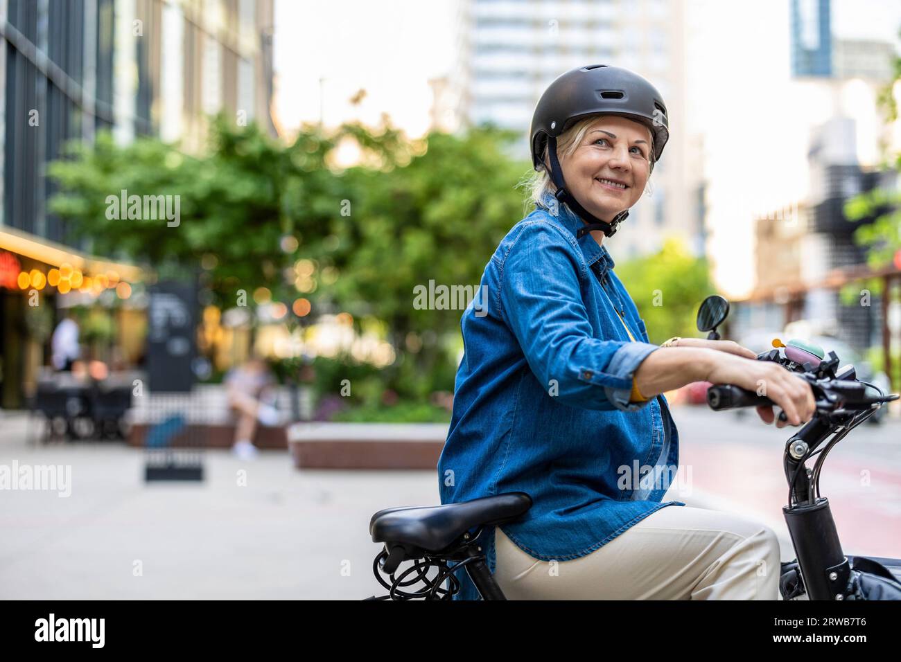 Ritratto di una donna anziana che indossa il casco mentre si va in bicicletta in città Foto Stock