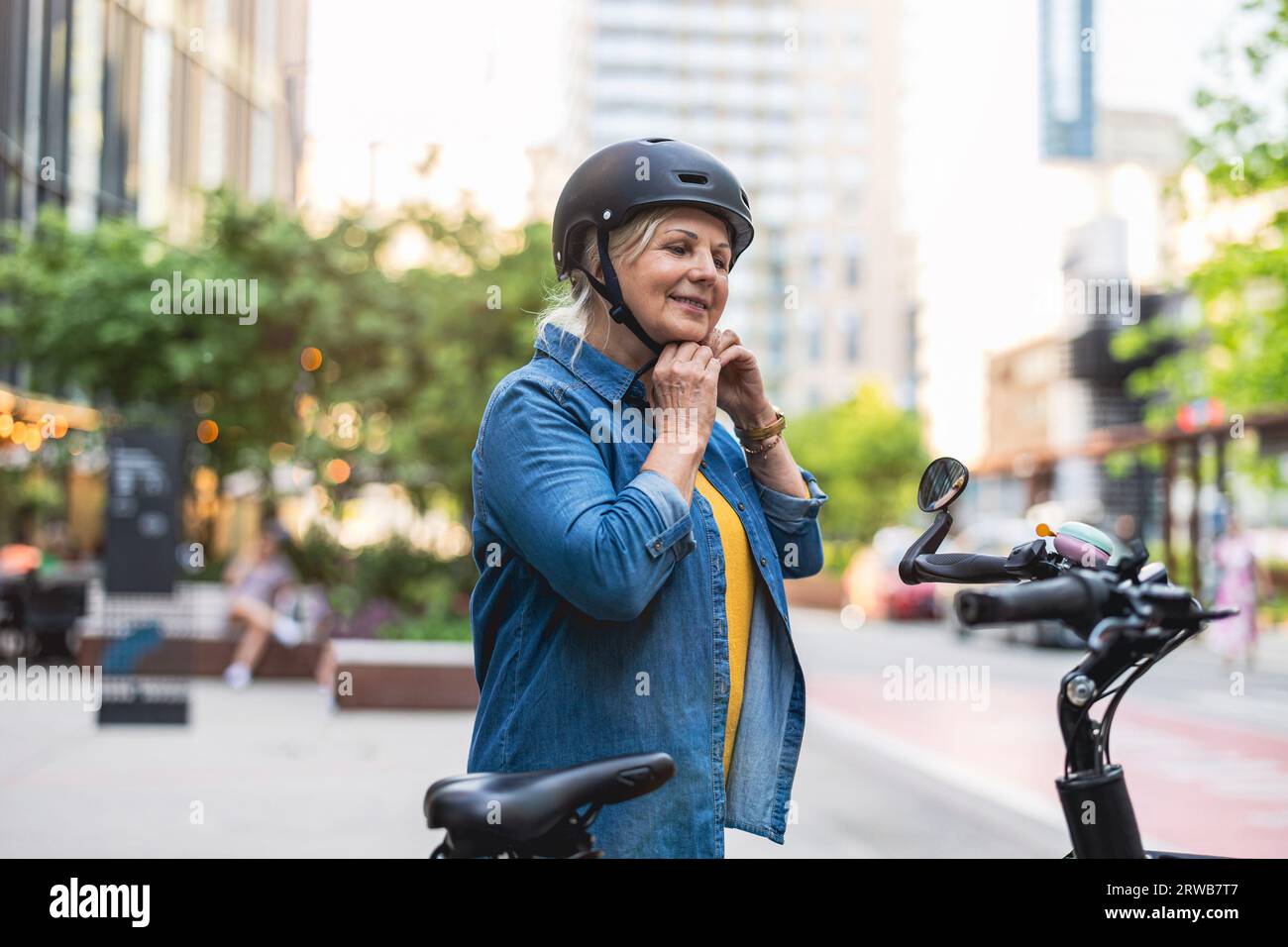 Ritratto di una donna anziana che indossa il casco mentre si va in bicicletta in città Foto Stock