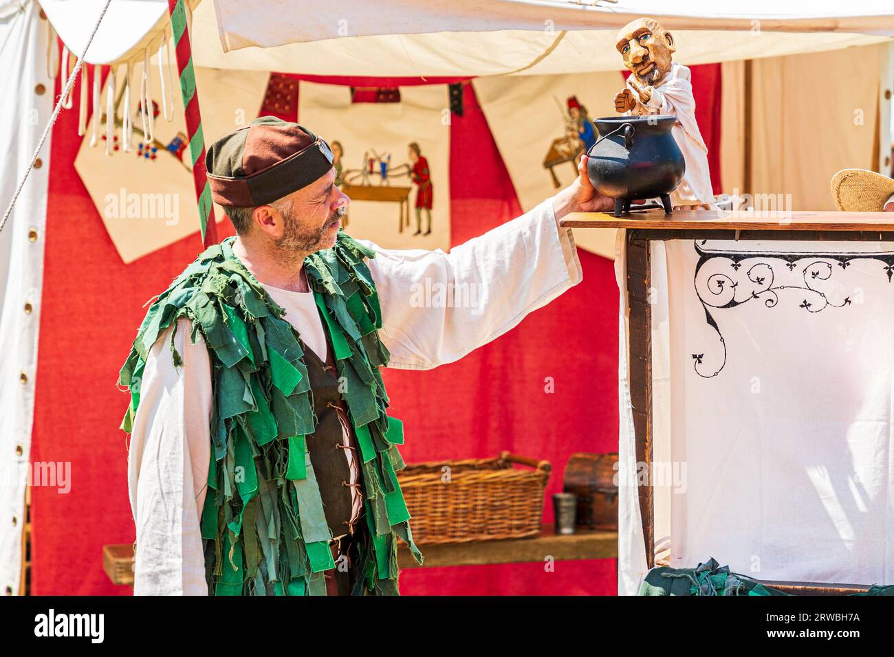 Burattinaio medievale in costume del periodo verde, esibendosi con burattino durante un evento di rievocazione a Sandwich Town nel kent in estate. Foto Stock