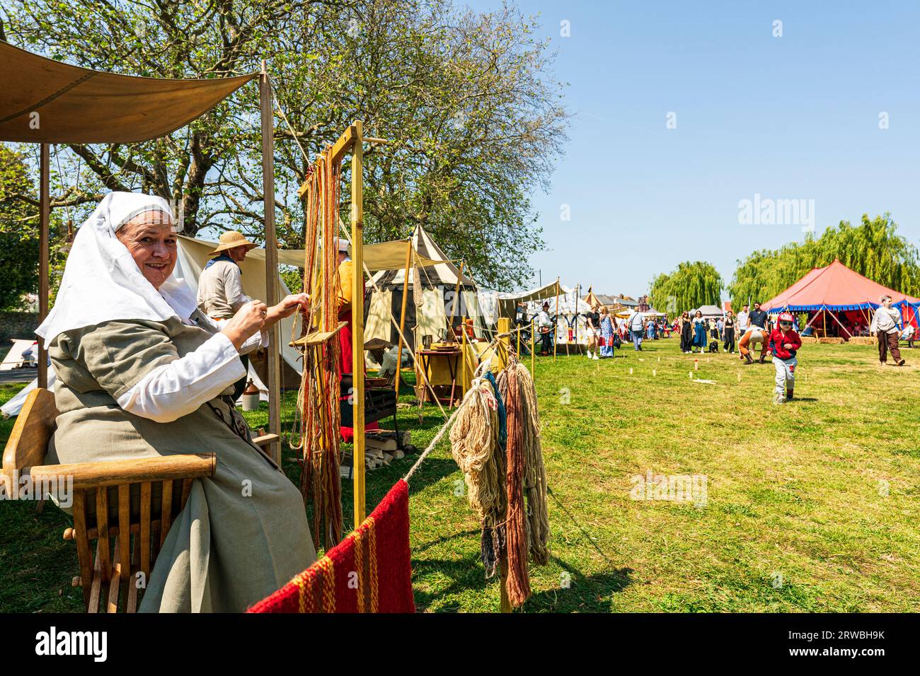 Donna in costume del periodo di mezza età, che lavora su un telaio tessendo fili di stoffa durante un evento di rievocazione medievale nella città di Sandwich nel kent. Foto Stock