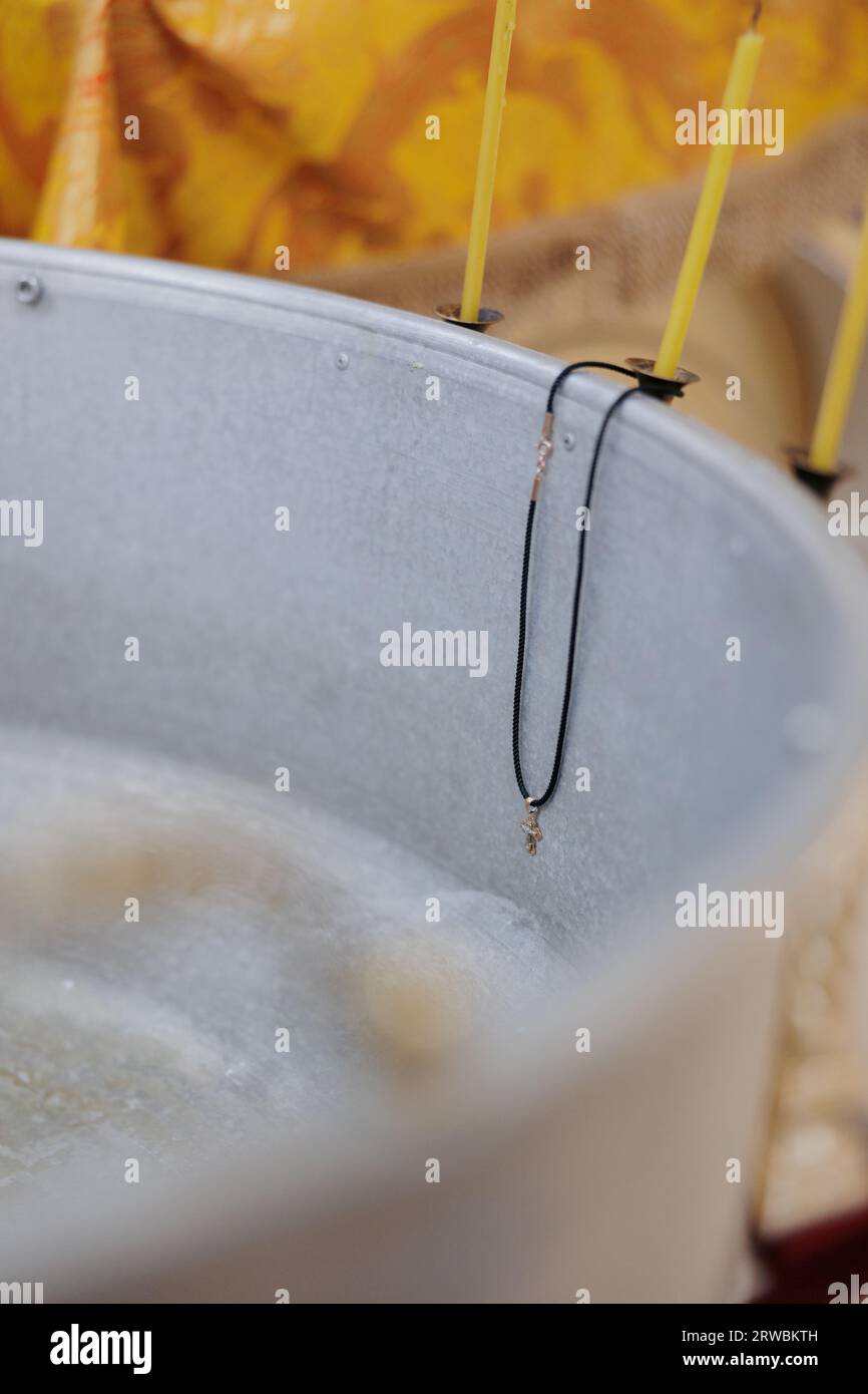 Fonte battesimale con acqua benedetta, croce pettorale e candele di cera. Rito battesimale per i neonati nella chiesa ortodossa. Primo piano. Foto Stock