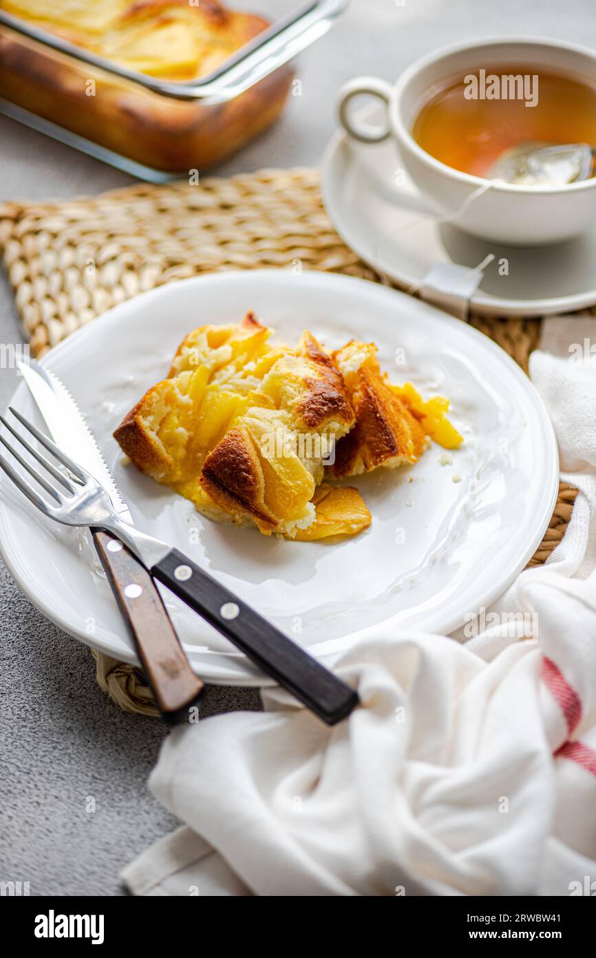 Angolo elevato di torta di pesca stagionale servita su piatto con forchetta e coltello e tazza di tè posta sul tavolo vicino al tovagliolo su sfondo sfocato Foto Stock
