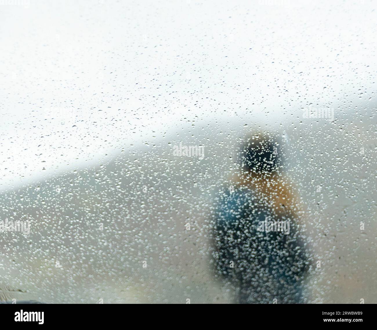 Attraverso il vetro con gocce di pioggia, vista di una persona anonima in piedi contro il crinale delle Alpi francesi in autunno Foto Stock