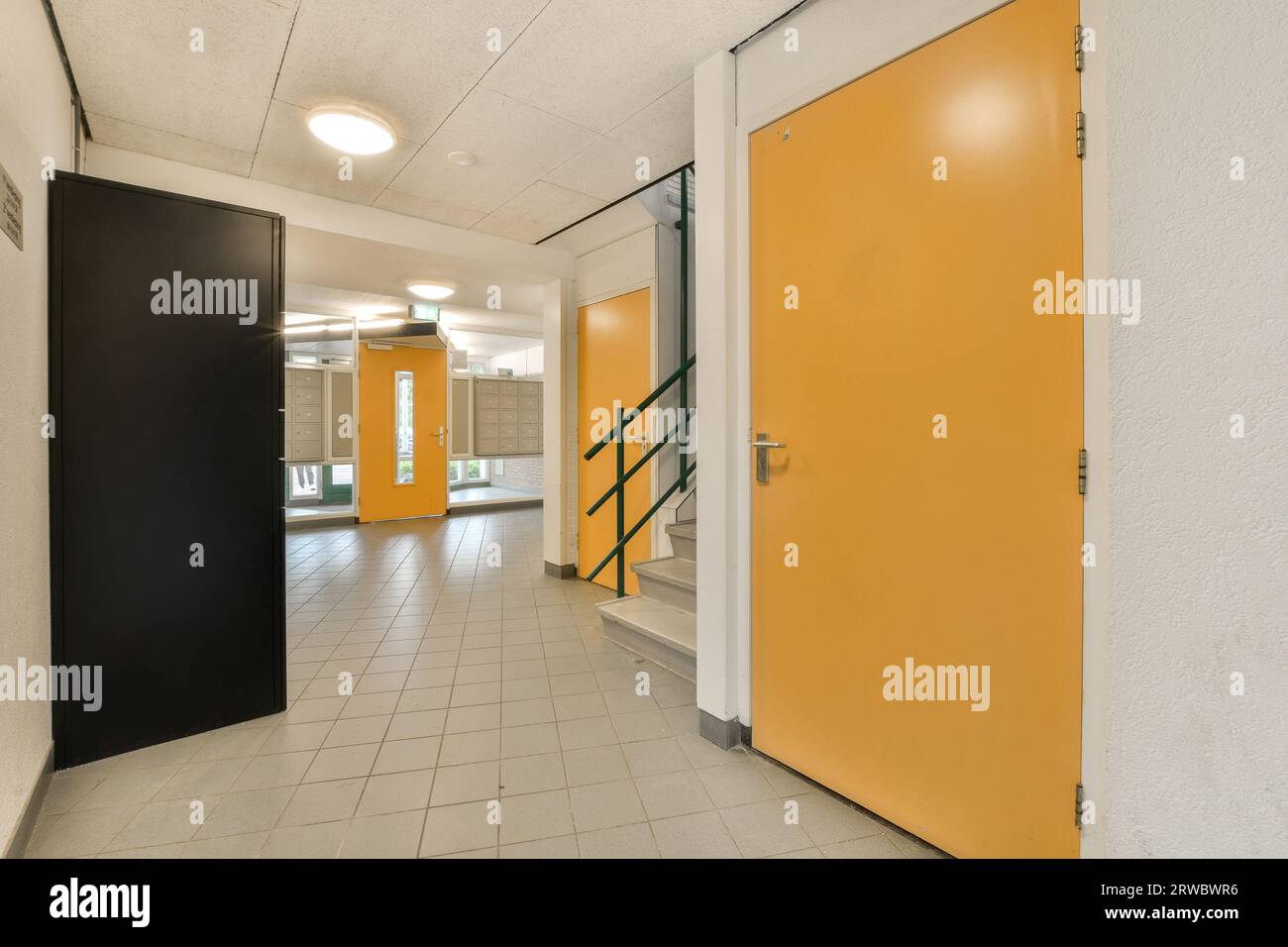 Interno di un lungo corridoio spazioso con porte gialle e pavimento piastrellato bianco in un moderno edificio di uffici illuminato Foto Stock