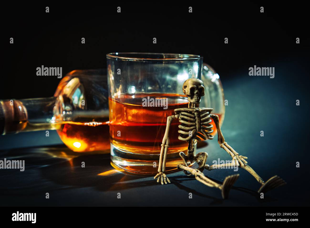 Lo scheletro umano è seduto con una bottiglia e un bicchiere di whisky in una stanza buia. Il concetto di lotta contro l'alcolismo. L'alcol uccide. Foto Stock