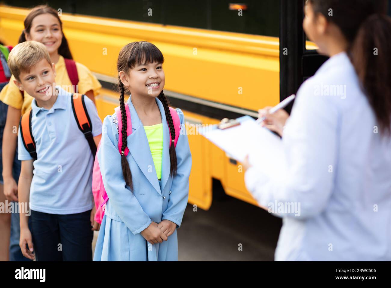 Insegnante di colore che aggiorna la lista di controllo dei bambini che entrano nello scuolabus Foto Stock