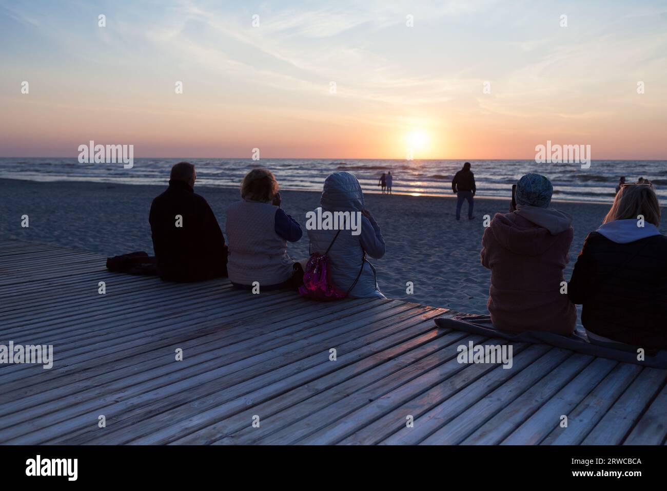 Gente che festeggia il tramonto sulla spiaggia in riva al mare. Foto Stock