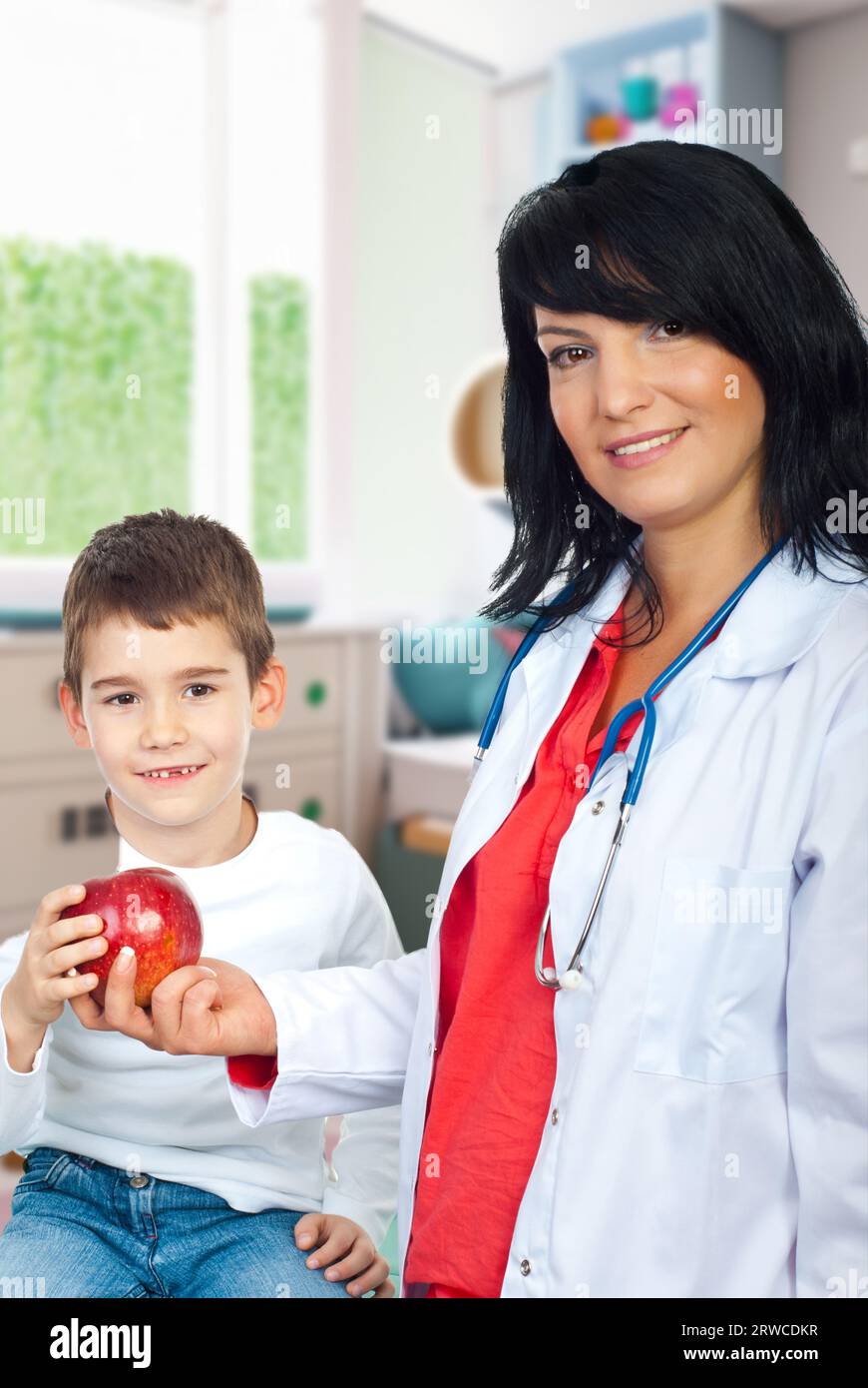 Felice medico donna dando una mela rossa a un bambino sorridente con denti mancanti Foto Stock