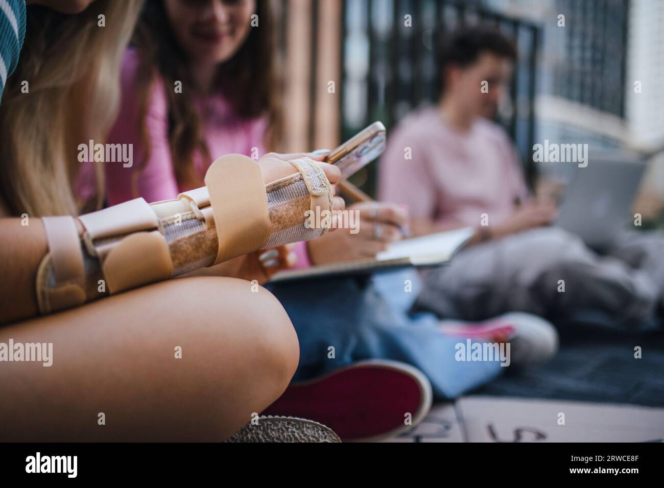 Primo piano della mano rotta di uno studente della generazione Z che studia all'aperto dopo la scuola. Foto Stock