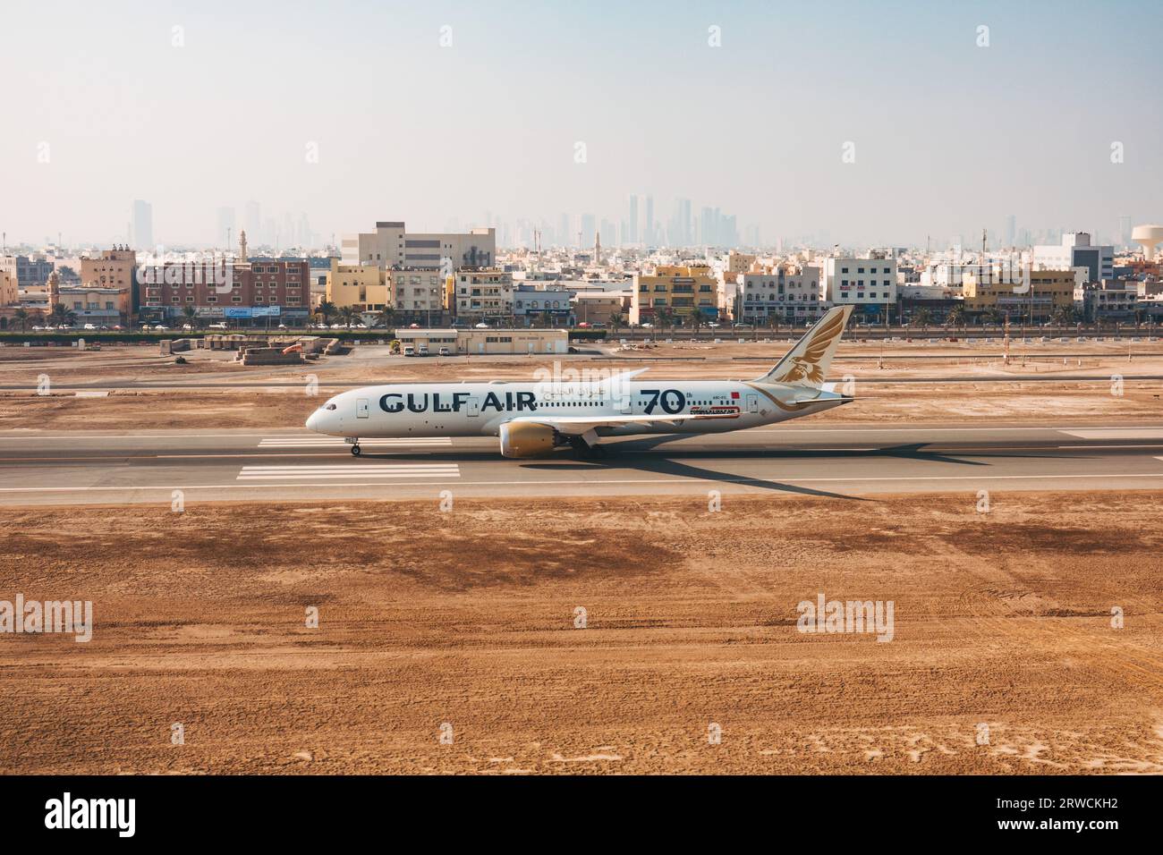 Un Boeing 787 Gulf Air sulla pista dell'aeroporto internazionale del Bahrain, Bahrain, con Muharraq e Manama City fotografate alle spalle Foto Stock