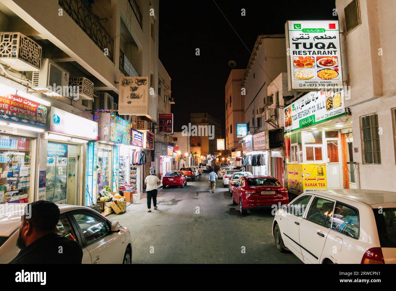 Le luci di ristoranti e negozi illuminano una strada di notte ad al Muharraq, un vecchio quartiere di Manama, capitale del Bahrain Foto Stock