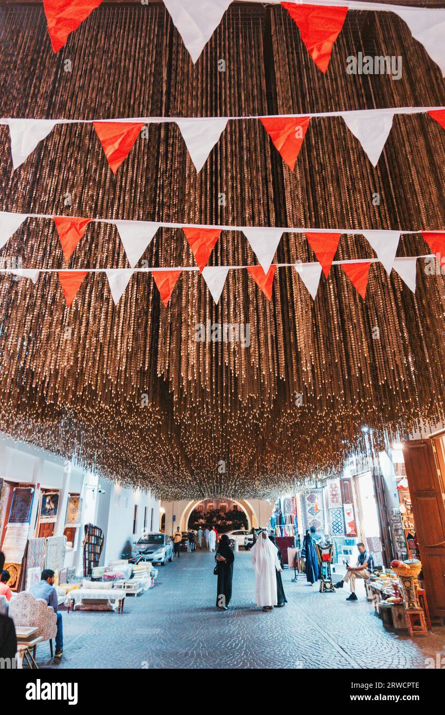 Aste sospese marrone formano un'installazione artistica all'interno del Manama Souq, Bahrain. Le bandiere rosse e bianche rappresentano i colori nazionali Foto Stock