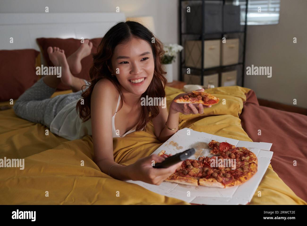 Una ragazza felice che mangia pizza e guarda film comici in tv quando passa la serata a casa Foto Stock