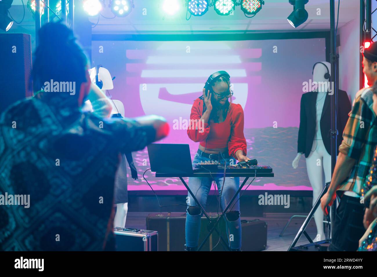Donna musicista che utilizza il controller dj mentre si esibisce sul palco in un nightclub. Disco jokey afroamericano che suona e mixa musica elettronica durante il concerto disco party nel club Foto Stock