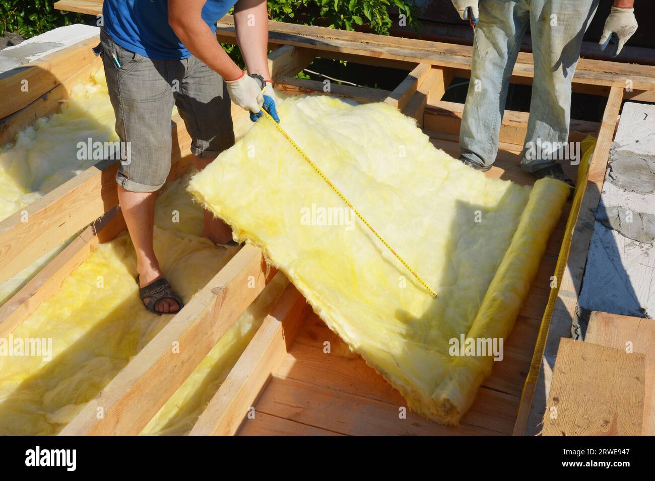 Isolamento mansardato con lana minerale. L'appaltatore di tetti misura il materiale isolante in lana minerale per il taglio durante l'isolamento del pavimento in soffitta. Foto Stock