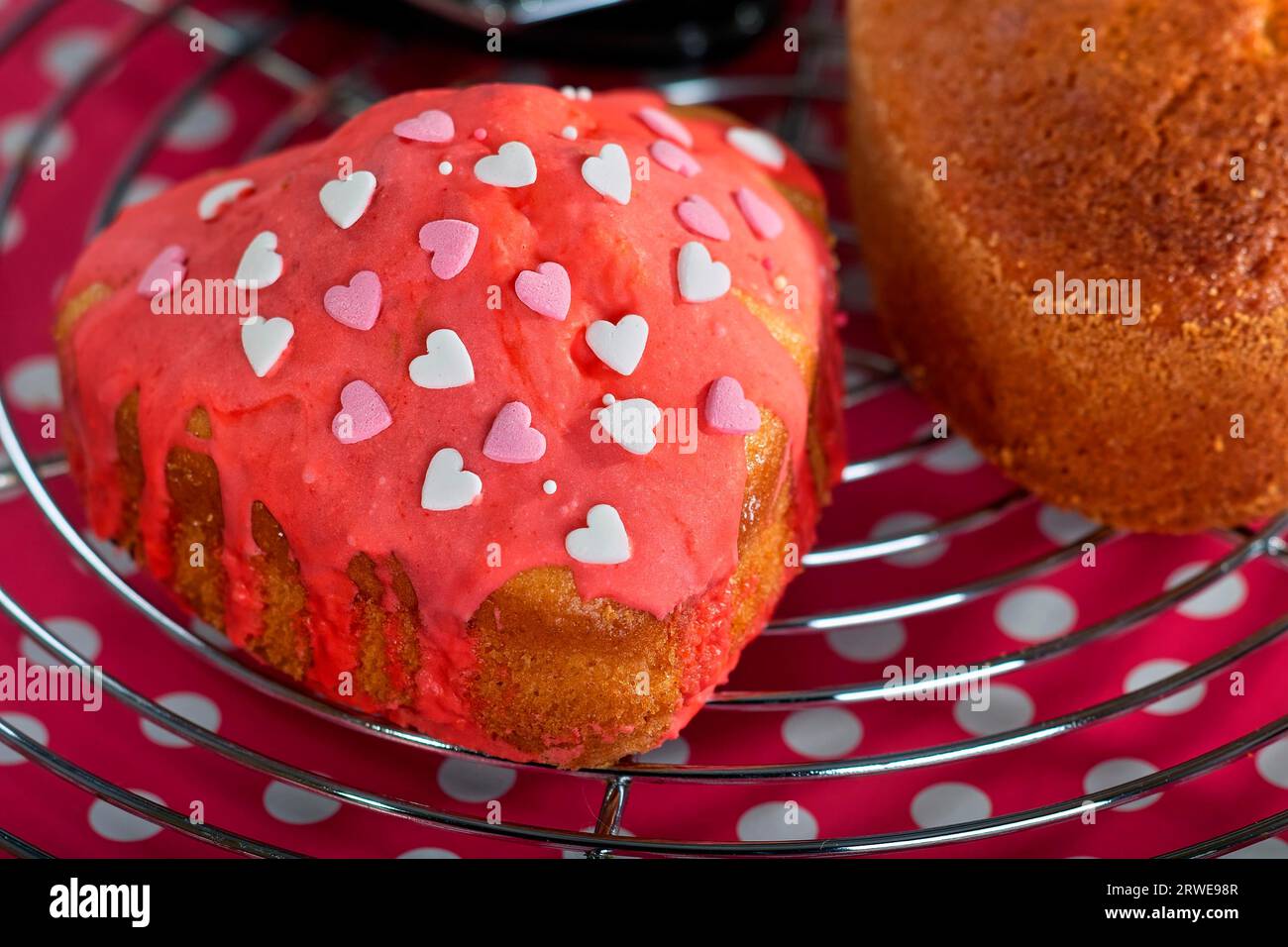 Piccola torta decorata con glassa e cuori in piedi su una griglia da forno Foto Stock