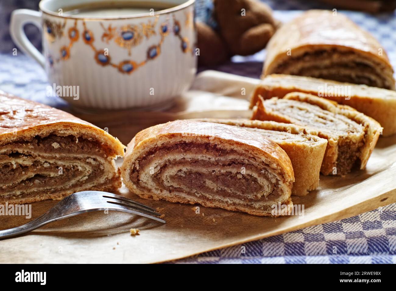 Nella torta di noci in primo piano su un piatto, sullo sfondo una tazza di caffè e un rotolo di noci tagliato Foto Stock