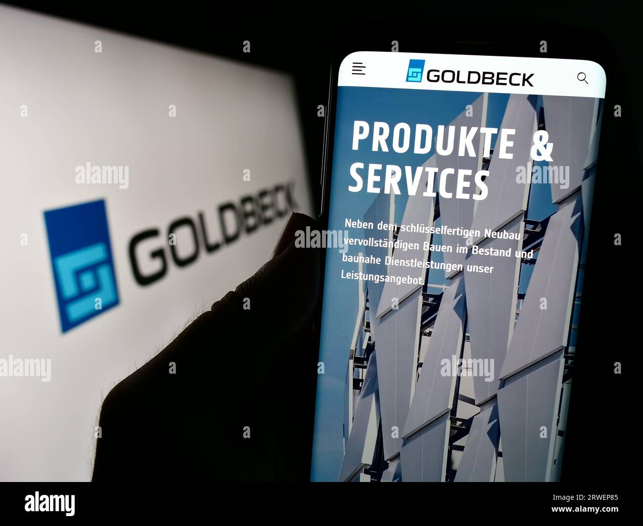 Persona in possesso di un cellulare con la pagina web della società tedesca di costruzioni Goldbeck GmbH sullo schermo davanti al logo. Concentrarsi sul centro del display del telefono. Foto Stock