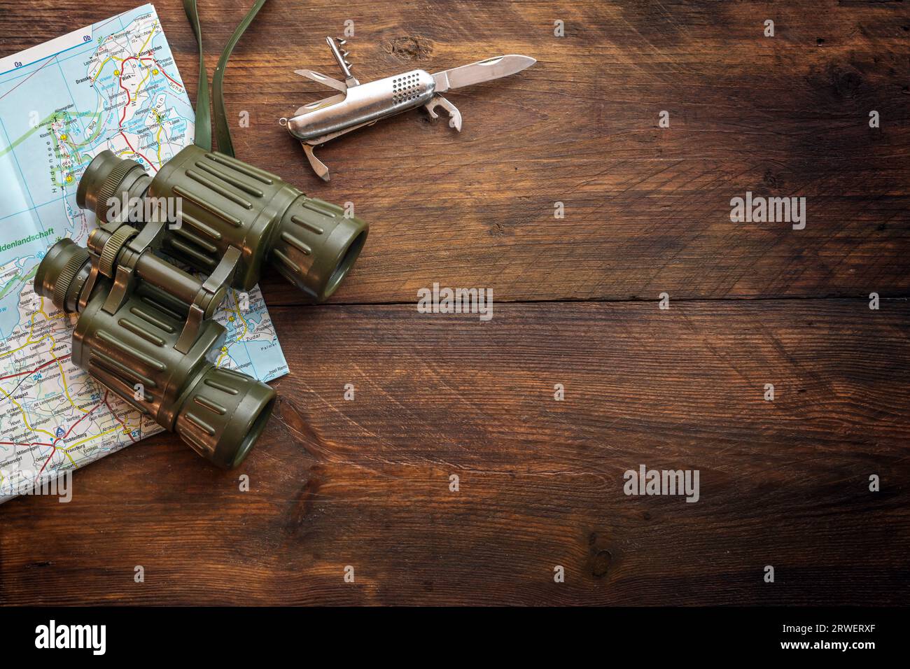 Binocolo, mappa e coltello tascabile su uno sfondo rustico scuro in legno, concetto di viaggio per trekking, escursioni e vacanze avventurose, vista dall'alto Foto Stock