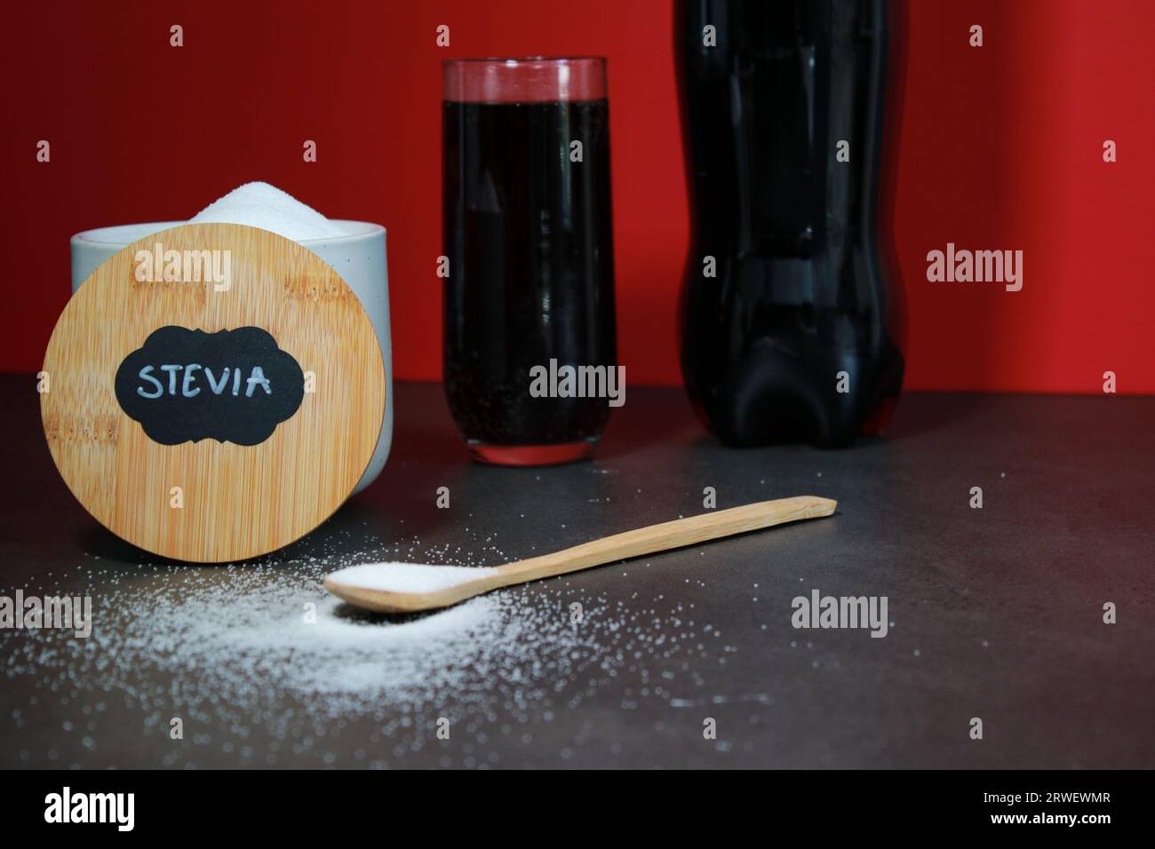 Un bicchiere di coca cola e dolcificante naturale con cucchiaio S, sfondo rosso Foto Stock