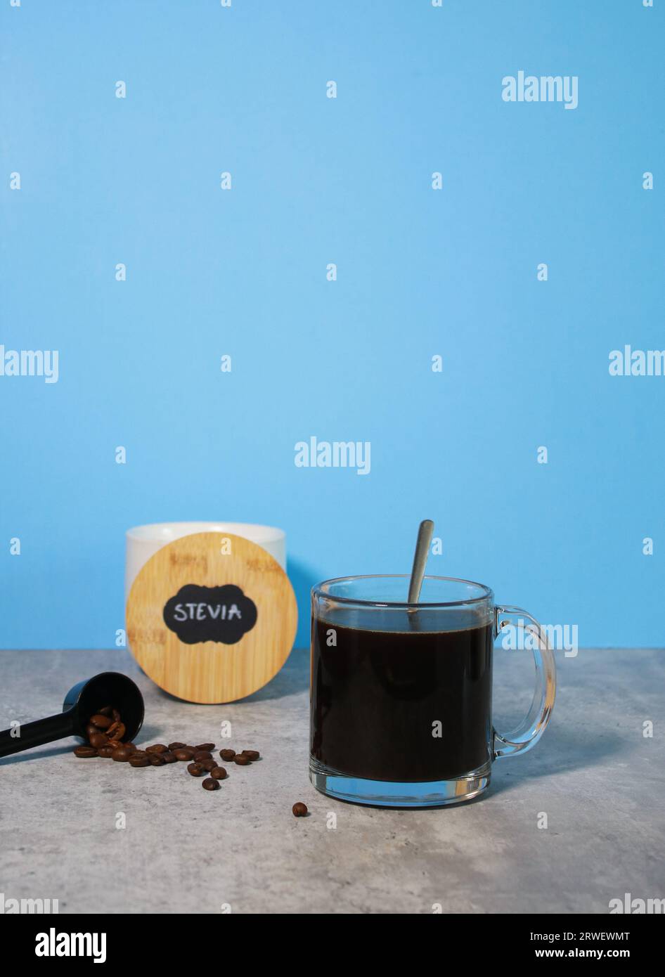 Un bicchiere di caffè nero e una ciotola con dolcificante stevia, sfondo blu Foto Stock