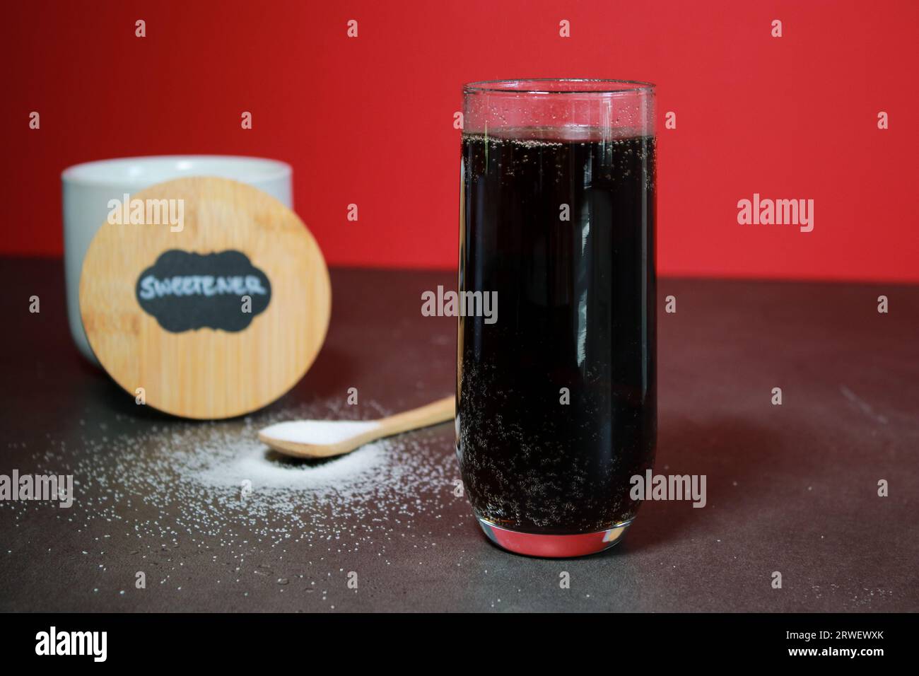 Un bicchiere di coca cola e dolcificante naturale con cucchiaio S, sfondo rosso Foto Stock