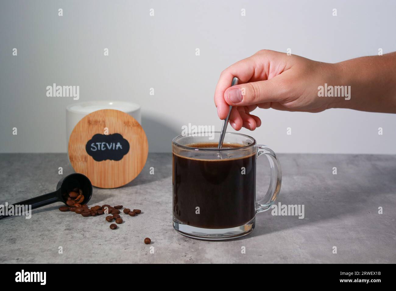 Dolcificante stevia con agitazione manuale da donna in caffè nero, sfondo grigio Foto Stock