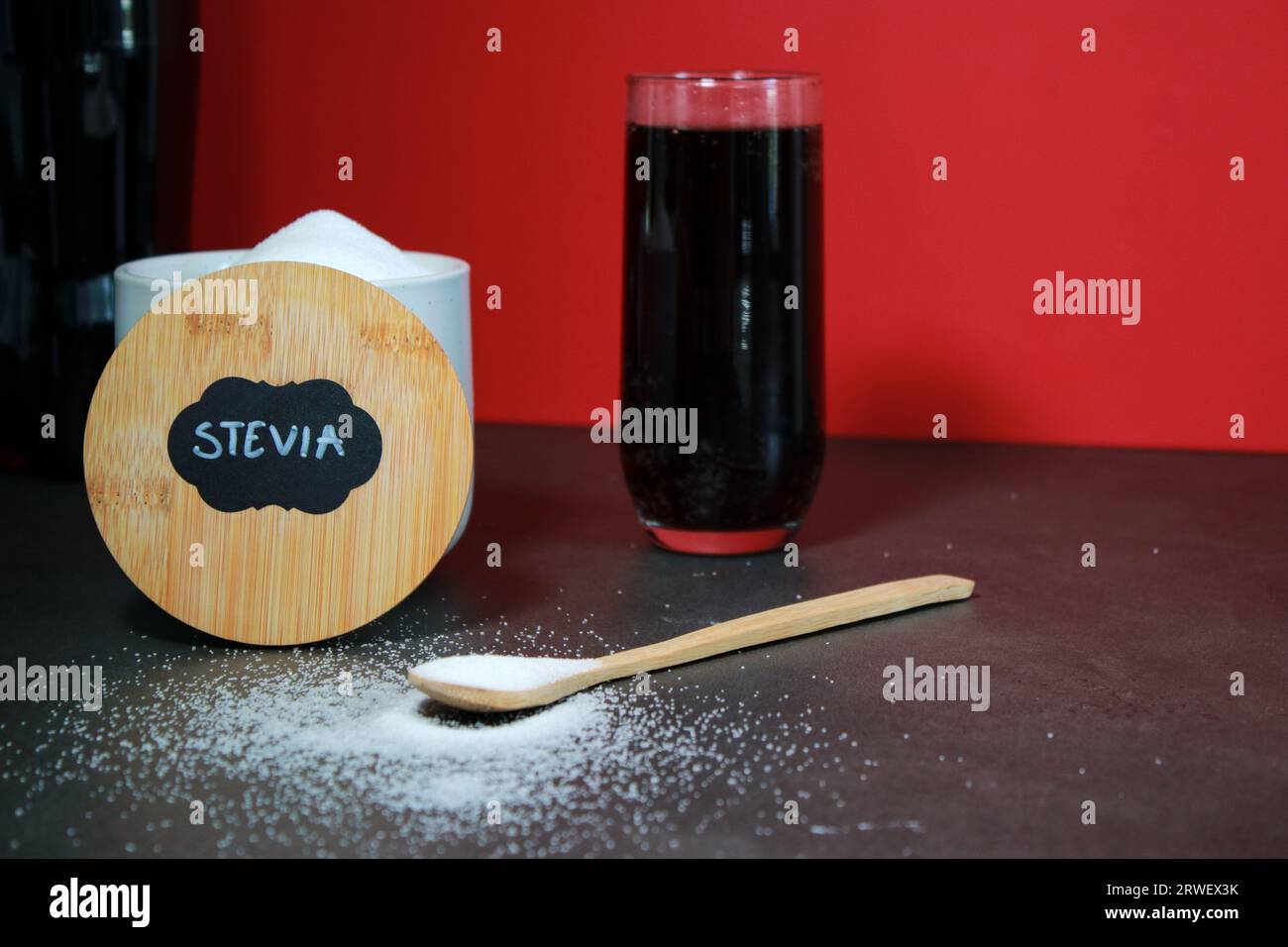 Un bicchiere di coca cola e dolcificante naturale con cucchiaio S, sfondo rosso Foto Stock