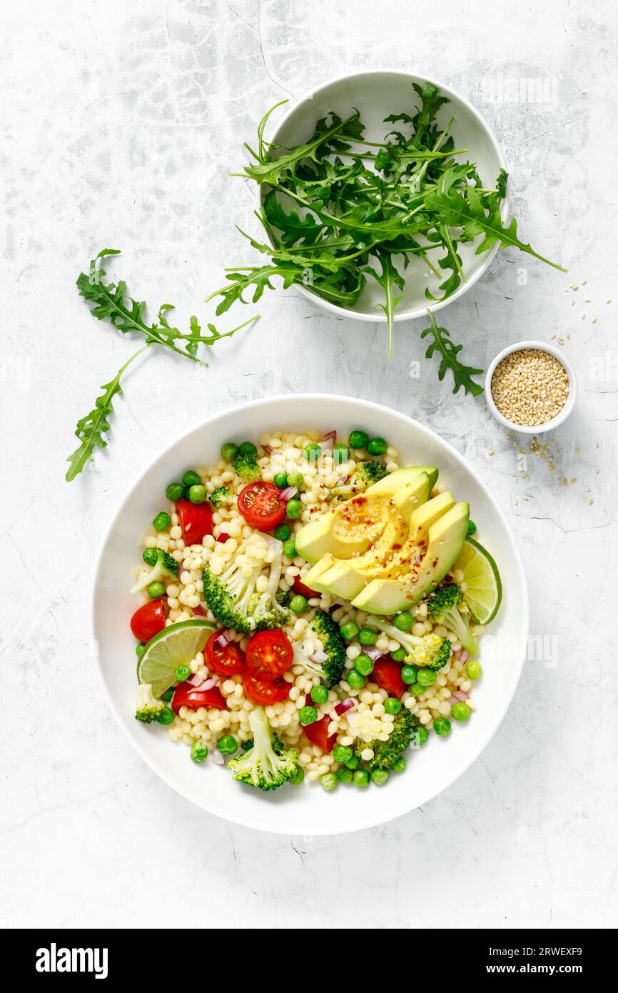 Insalata di couscous con broccoli, piselli verdi, pomodori, avocado e rucola fresca. Cibo vegetariano a base vegetale naturale sano per pranzo, cucina israeliana, Foto Stock