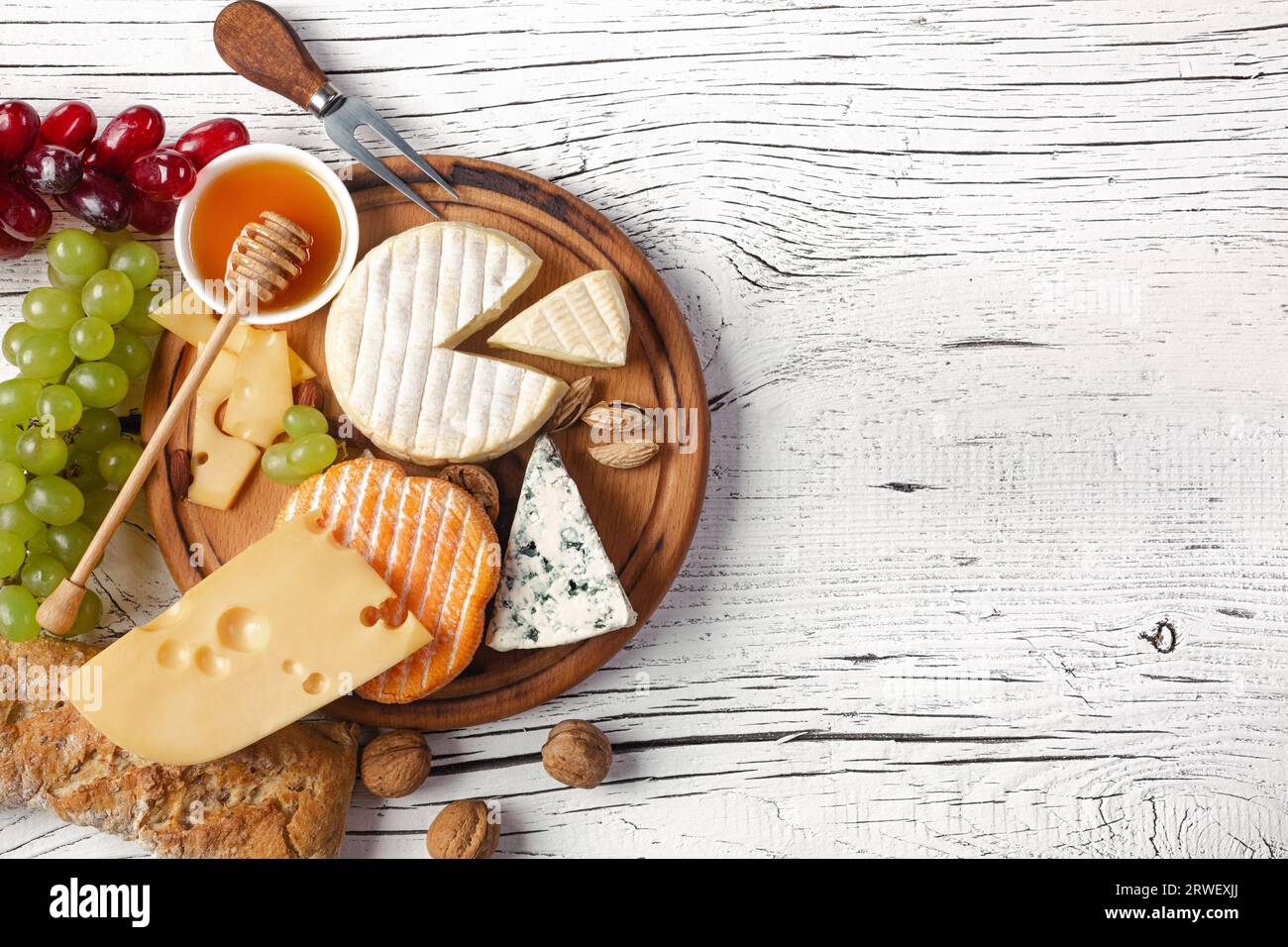 Formaggio, uva, miele e noci su tagliere e tavolo in legno bianco. Vista dall'alto. Foto Stock