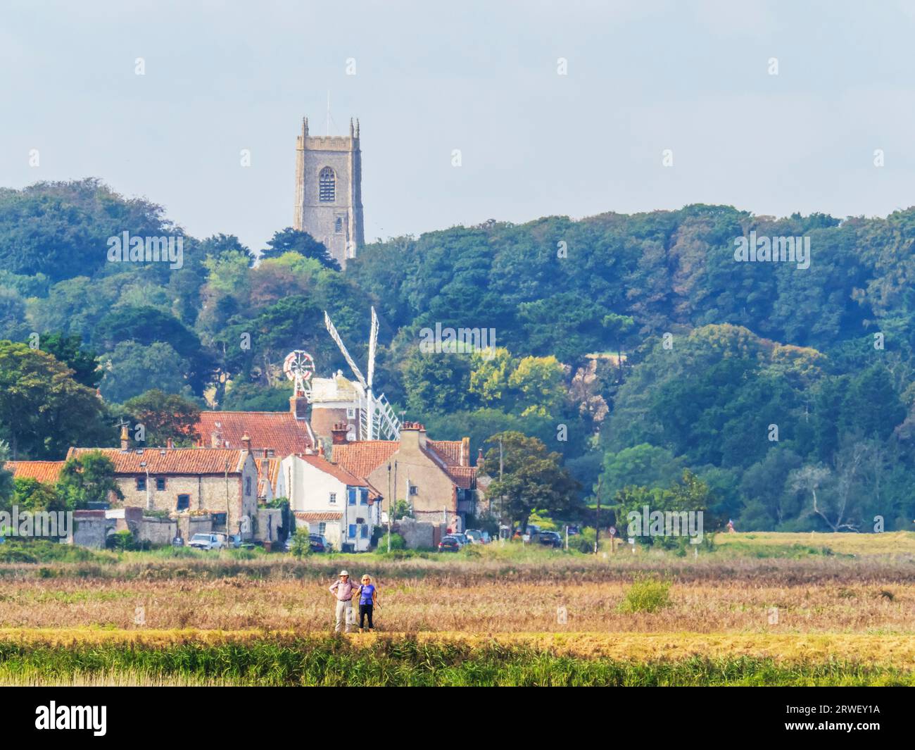 Il mulino a vento di Cley Next the Sea, con la chiesa di Blakeney alle spalle, Norfolk, Regno Unito, con un paio di passeggiate. Foto Stock