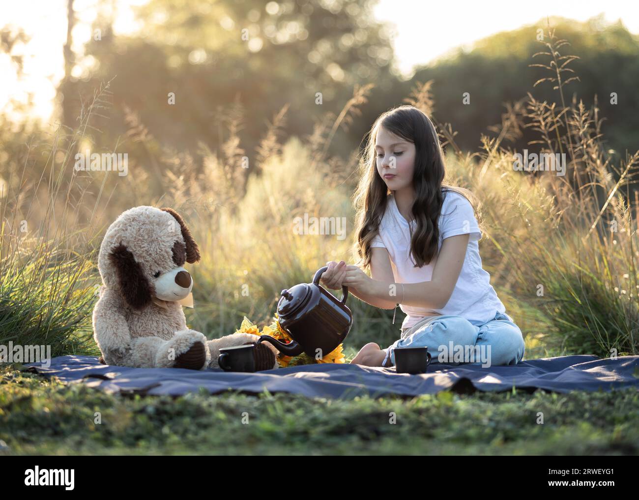 La giovane ragazza caucasica e il suo orsacchiotto fanno un tè all'aperto in natura Foto Stock