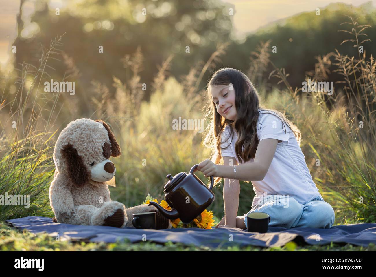 La giovane ragazza caucasica e il suo orsacchiotto fanno un tè all'aperto in natura Foto Stock