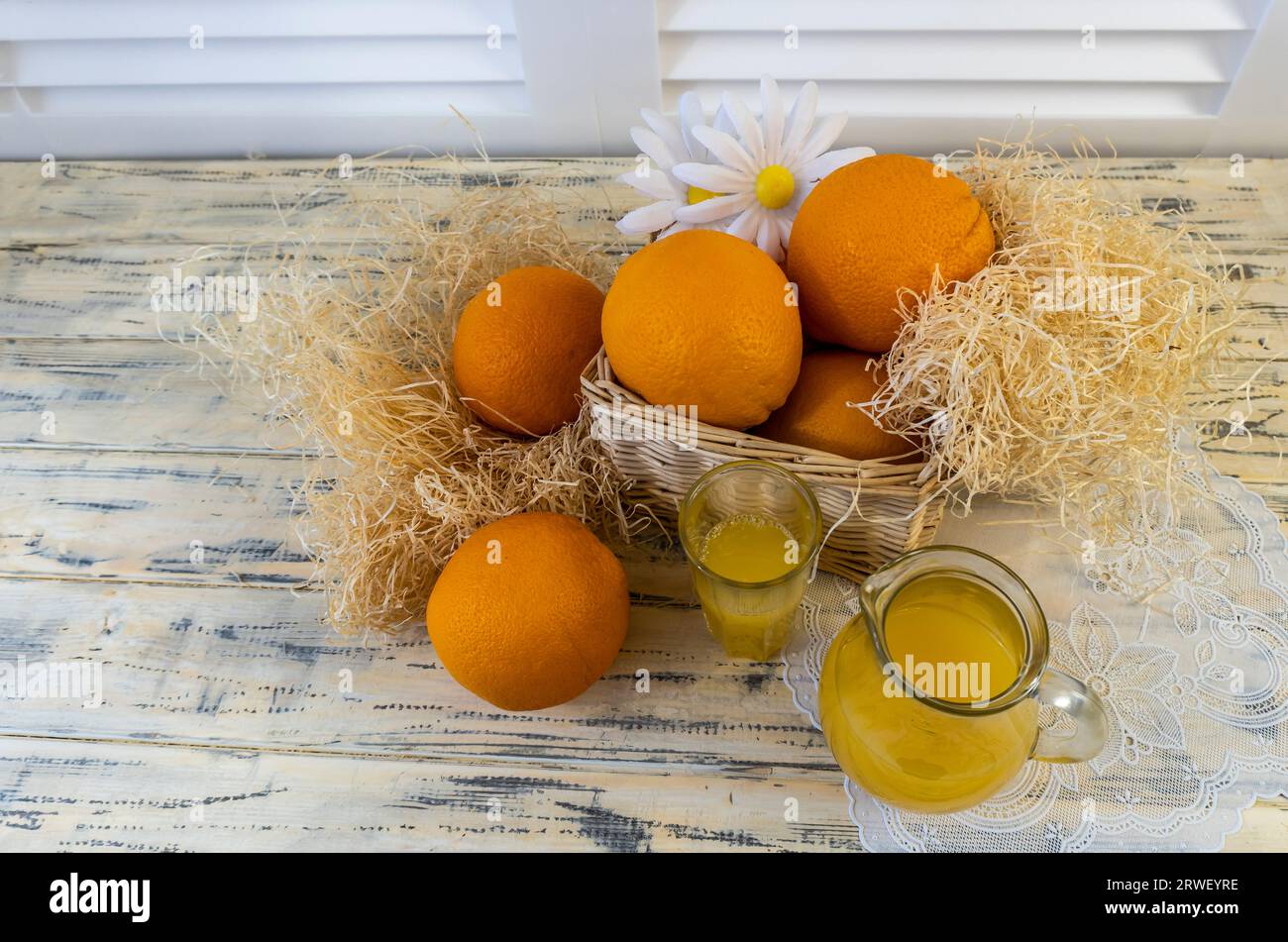 Vita morta con arance, cesto e brocca di vetro con succo su vecchio sfondo di legno luminoso Foto Stock