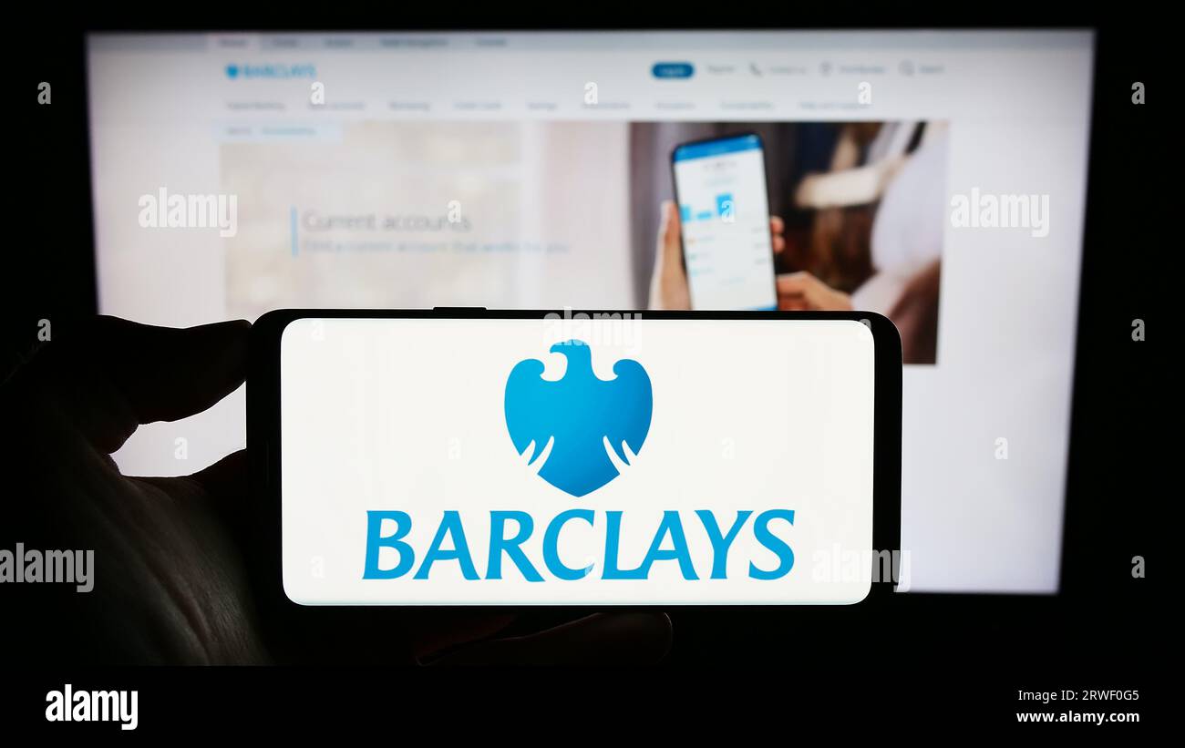 Persona che tiene il cellulare con il logo della banca universale britannica Barclays plc sullo schermo di fronte alla pagina Web aziendale. Concentrarsi sul display del telefono. Foto Stock