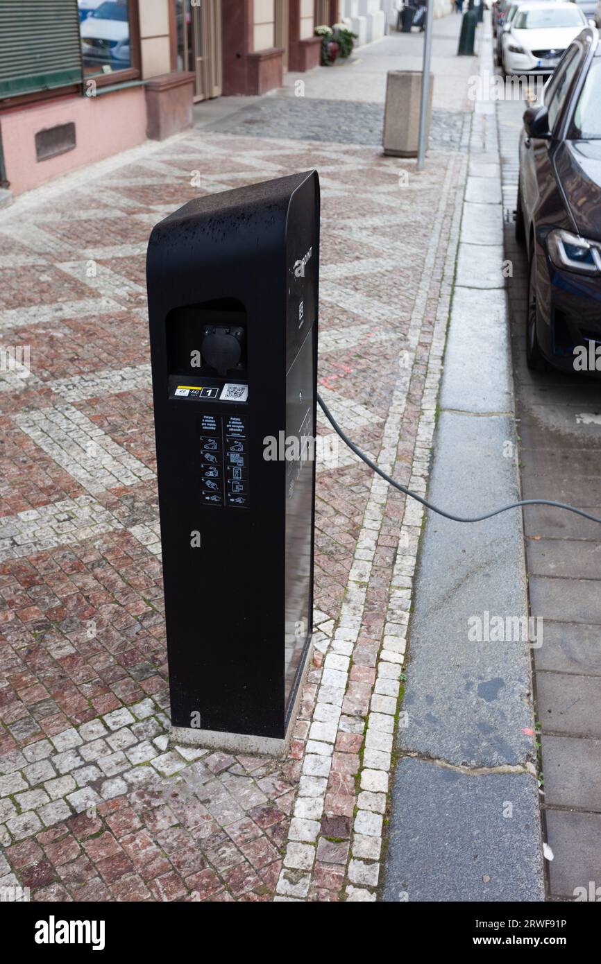 Una stazione di ricarica nera con il cavo collegato a un'auto nera parcheggiata. Foto Stock