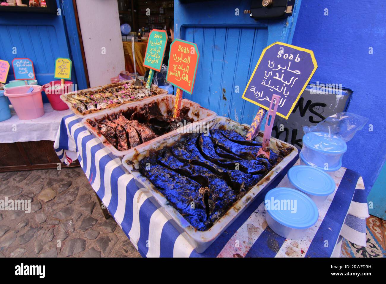 Una vivace e colorata scena del souk Chefchaouen con sapone nero marocchino in vassoi su un panno a righe blu e bianco e altri souvenir in vendita Foto Stock
